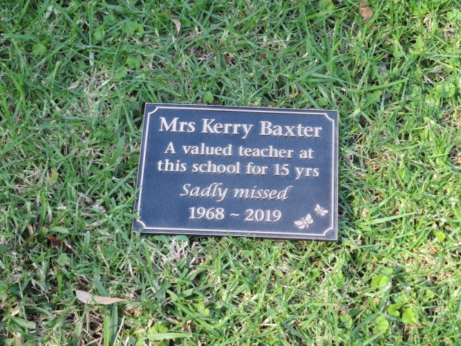 rectangle bronze plaque with memorial inscription for a person. Layed on grass