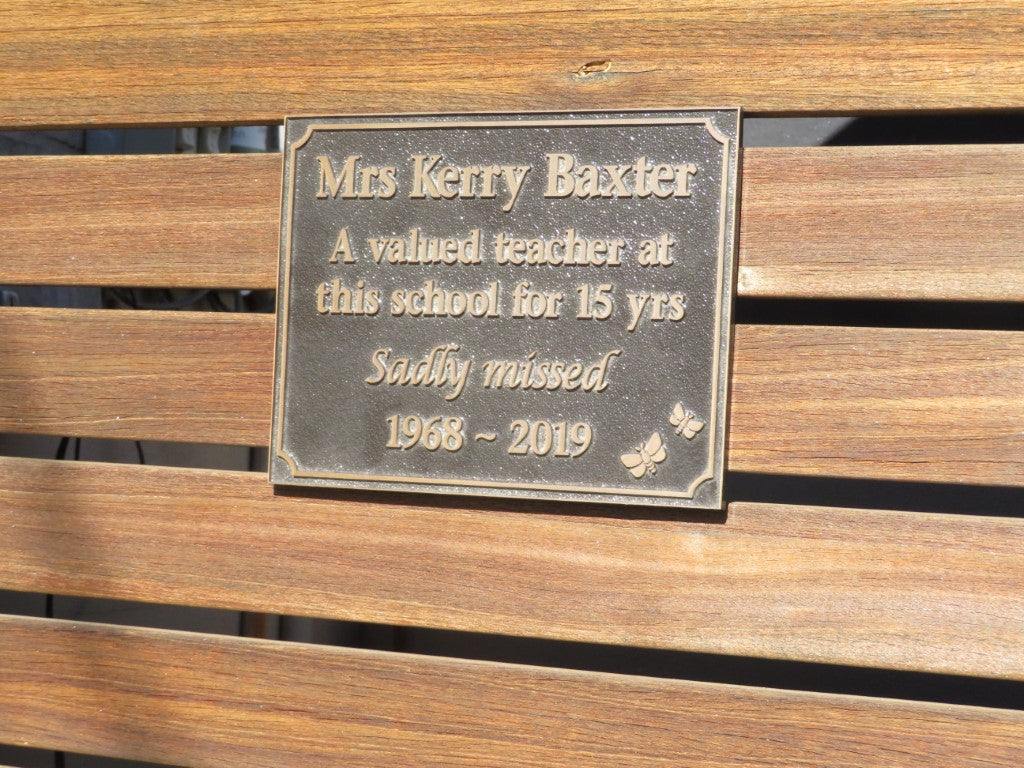 rectangle bronze plaque with memorial inscription for a person. Installed on a wooden bench