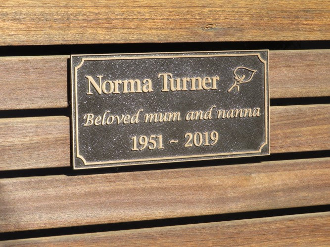 bronze plaque with memorial inscription for a person. The plaque is attached to wood planks on a bench